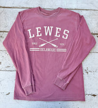 Load image into Gallery viewer, Flat lay of a washed maroon Comfort Colors long sleeve t-shirt with "LEWES SINCE 1631 DELAWARE" text and crossed white oars graphic on a distressed white wooden background.