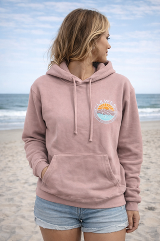 Person wearing a pink hoodie with a beach graphic on a sandy beach.