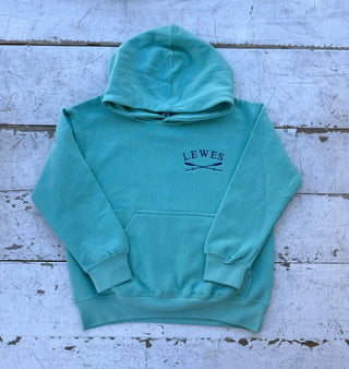 Front view of a vibrant green children's pullover hoodie with an embroidered 'LEWES' logo and crossed oars on the chest, featuring a kangaroo pocket and hood, laid on a distressed white wooden surface.