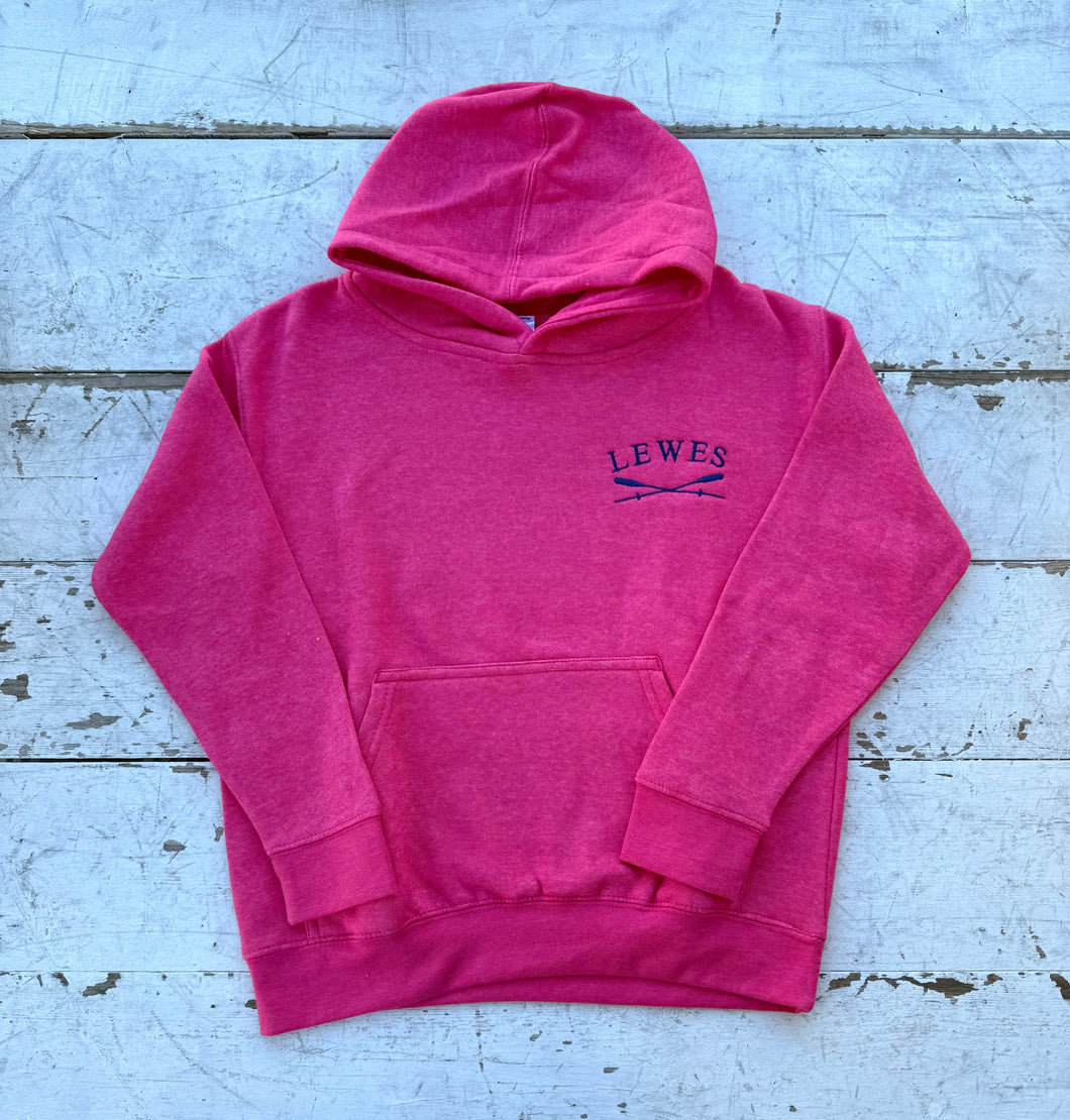 Front view of a vibrant pink children's pullover hoodie with an embroidered 'LEWES' logo and crossed oars on the chest, featuring a kangaroo pocket and hood, laid on a distressed white wooden surface.