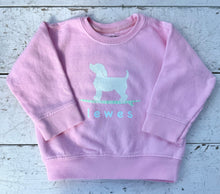 Load image into Gallery viewer, Pink long-sleeve kids&#39; sweatshirt featuring a white graphic of a dog on a surfboard and &quot;Lewes&quot; text, displayed on a distressed white wooden surface.
