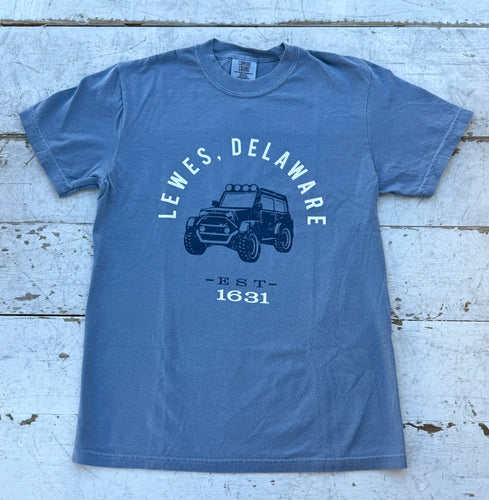 A faded slate blue Comfort Colors t-shirt with a dark blue graphic featuring 'Lewes, Delaware' in an arc above an off-road utility vehicle, and 'EST - 1631' below.