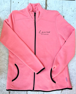 Pink full-zip fleece jacket featuring 'Lewes Delaware' text, black zipper, black trim on pockets, cuffs, and hem, laid flat on a distressed white wooden surface.