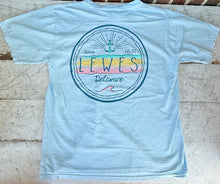 Load image into Gallery viewer, Back view of a light blue short-sleeve t-shirt featuring a circular graphic with &quot;Lewes Delaware Since 1631&quot; text, an anchor, and pastel yellow, pink, and teal waves, laid flat on a rustic white wooden surface.
