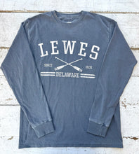 Load image into Gallery viewer, Flat lay of a washed navy Comfort Colors long sleeve t-shirt with &quot;LEWES SINCE 1631 DELAWARE&quot; text and crossed white oars graphic on a distressed white wooden background.
