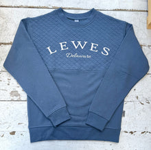Load image into Gallery viewer, Steel blue quilted crew neck sweatshirt featuring &quot;Lewes Delaware&quot; in white text, laid flat on a distressed white wooden surface.
