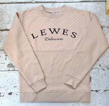 Load image into Gallery viewer, Tan quilted crew neck sweatshirt featuring &quot;Lewes Delaware&quot; in white text, laid flat on a distressed white wooden surface.
