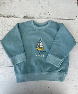 Teal blue toddler crewneck sweatshirt with a colorful sailboat and 'Lewes' graphic, displayed flat on a white distressed wooden surface.